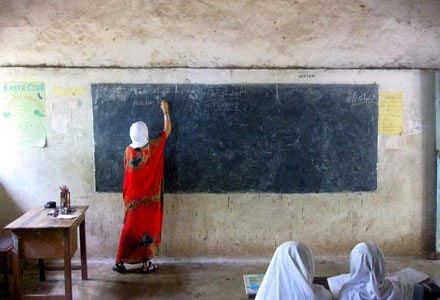 A woman writes on a chalkboard while students watch from behind