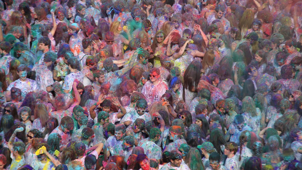 Powders of blue, pink, yellow, green and orange fall on a crowd of students wearing white shirts