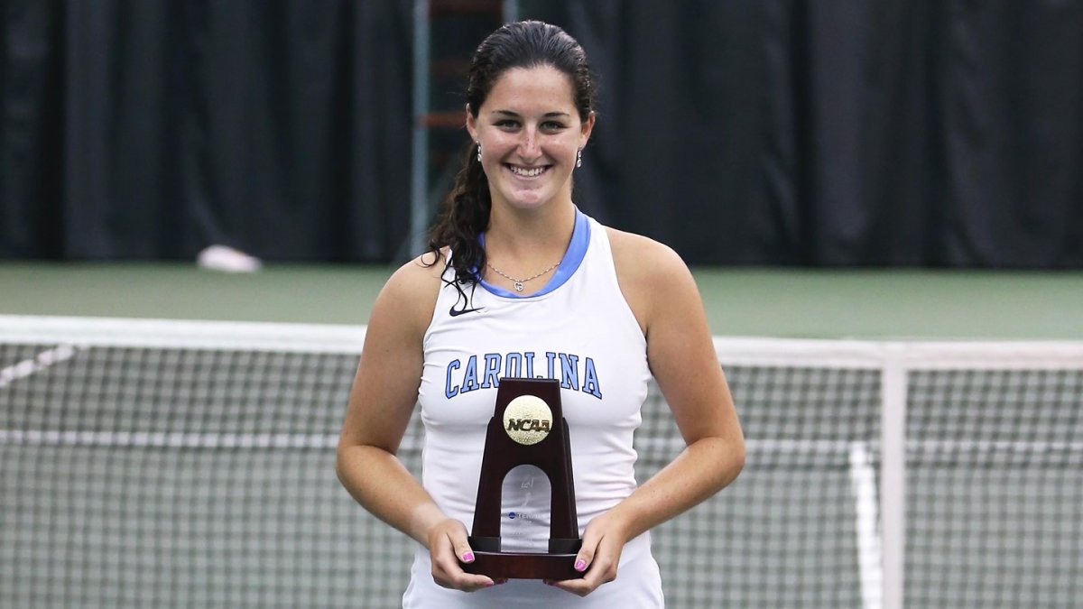 Jamie Loeb stands on a tennis court and holds an NCAA championship trophy