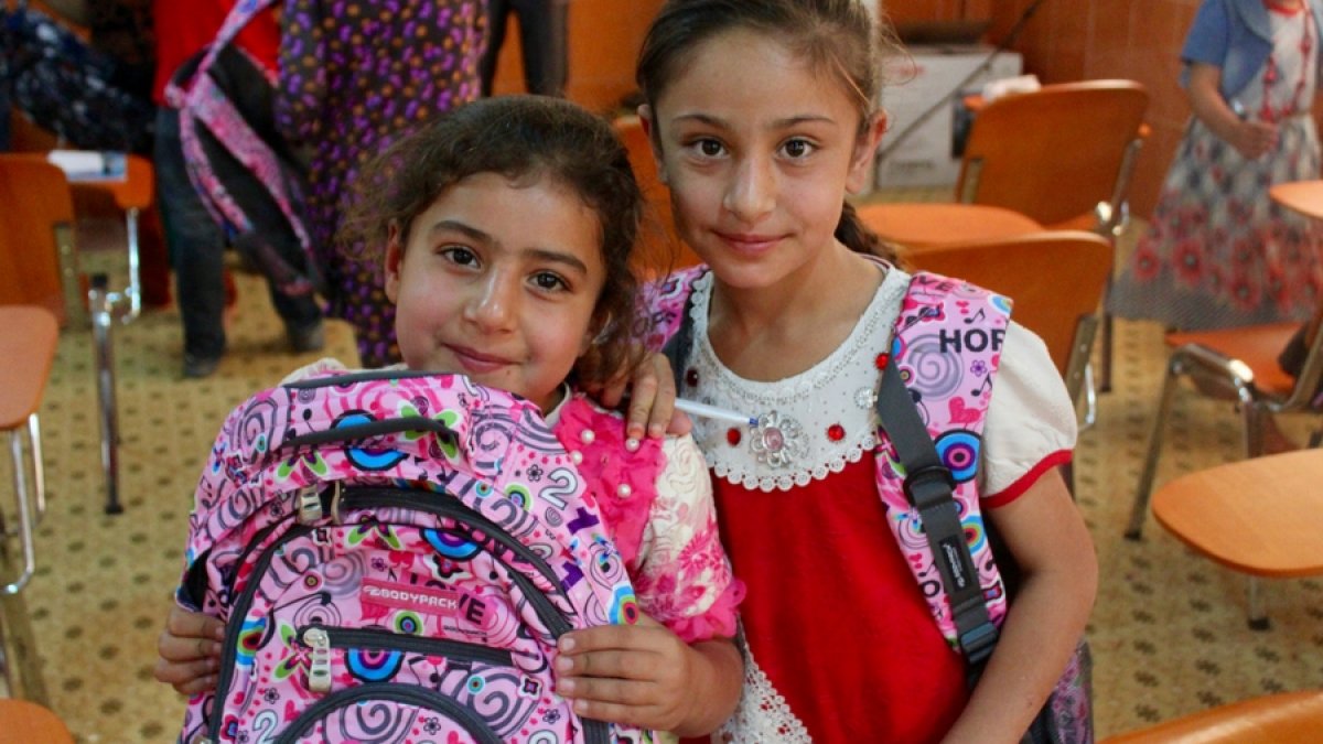 Two girls stand wth the backpacks they were given.