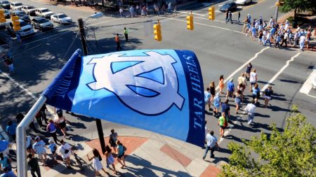 People walk along Chapel Hill's Franklin Street under a U.N.C. flag flying from a building.