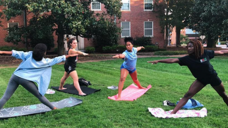 Four female student perform yoga on the lawn outside a Carolina residence hall.