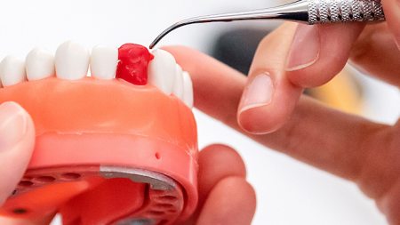 A student practices a dental procedure on a teeth mold.