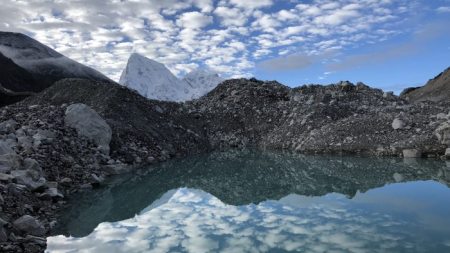 Early morning clouds are reflected in a blue pool on the Ngozumba glacier in the Gokyo Valley of Nepal, with the twin peaks of Cholatse and Arakam Tse visible in the background.
