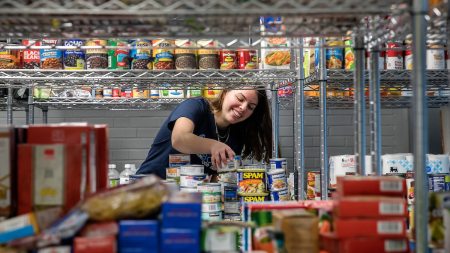 A female student places cans on a shelf at a food bank.