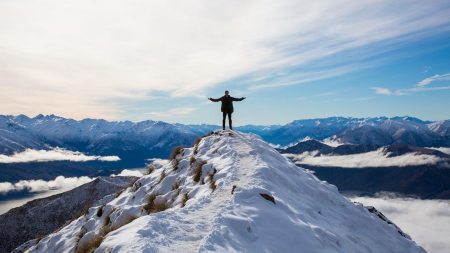 Distant shot of student standing with arms raised on top of a mountain