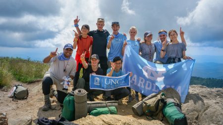 A group of students abroad holds up a Carolina flag for the camera