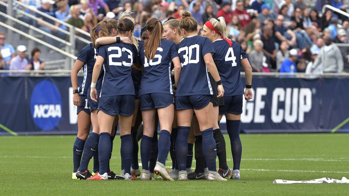 Members of the women's soccer team huddle on the field