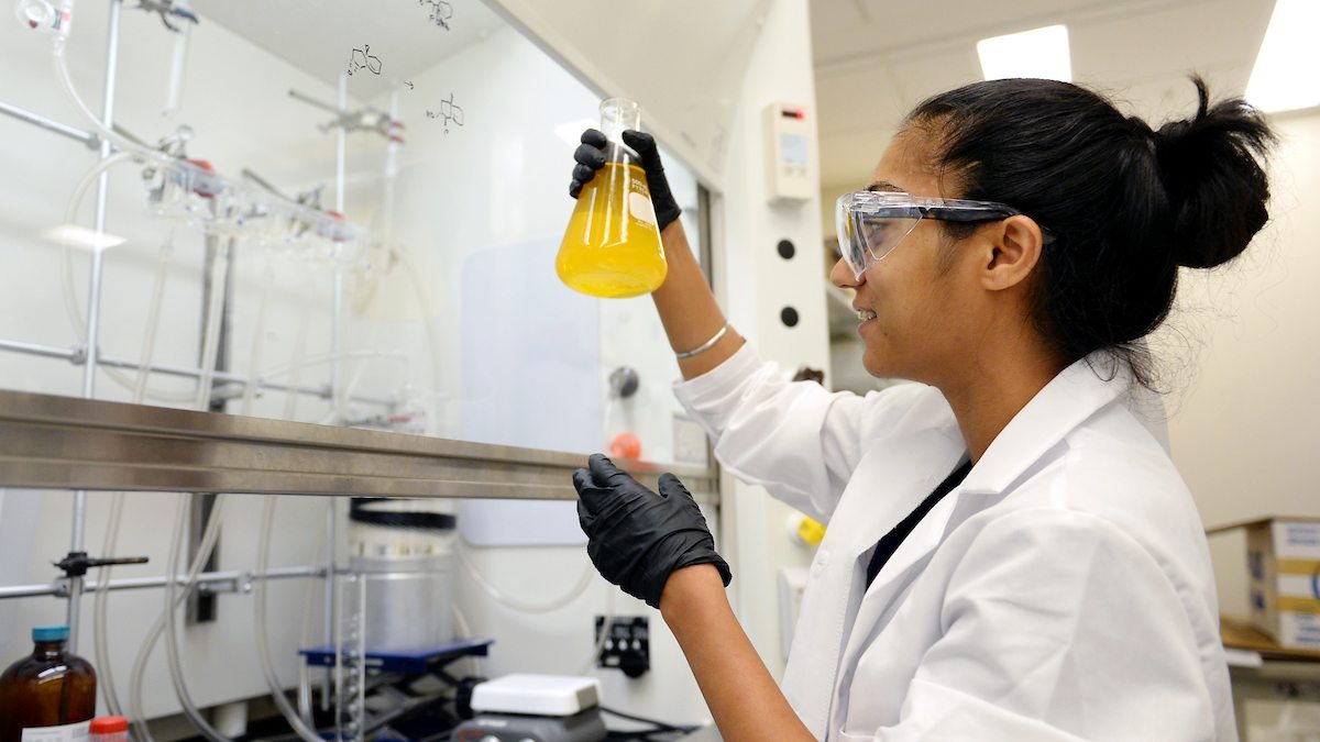 A woman holds a beaker in a research lab.