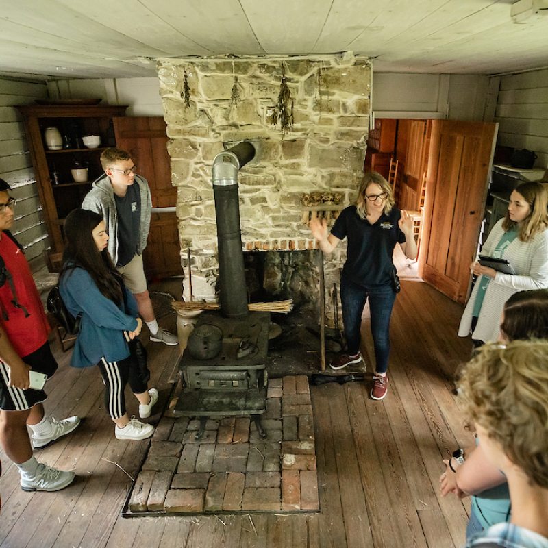 Students stand in the Duke Homestead State Historic Site listening to a speaker.