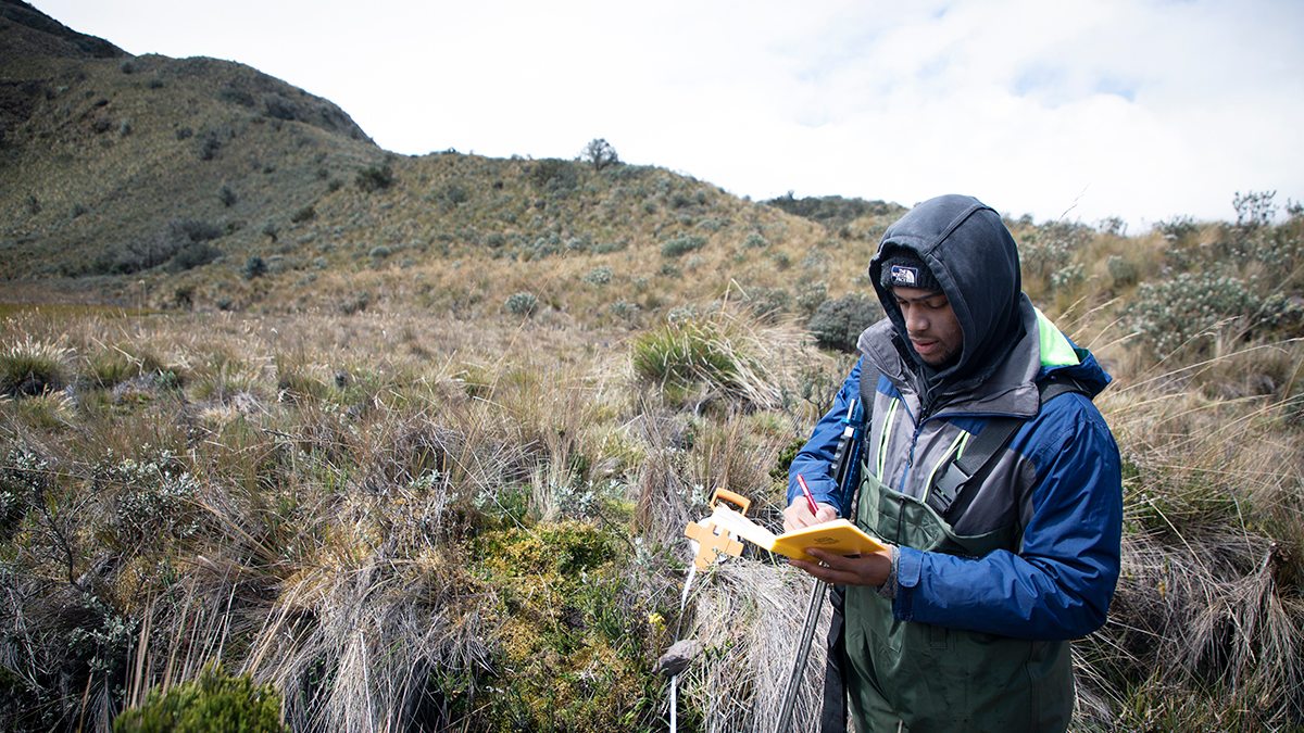 student takes notes in a field doing research.