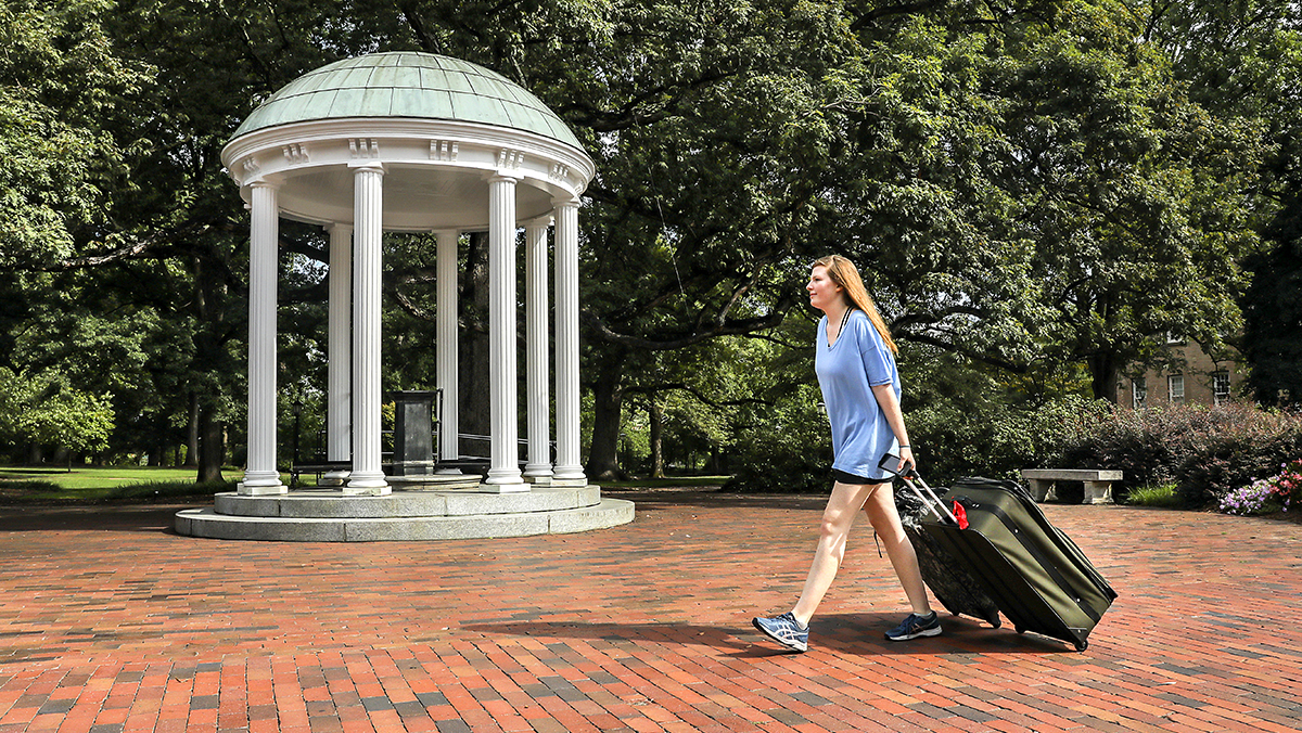A student rolls their suitcase past the Old Well during move-in