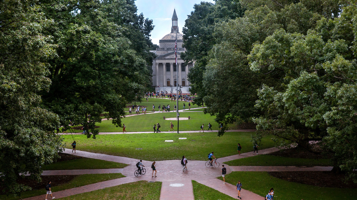 Student walk on Polk Place with Wilson Library in the background.