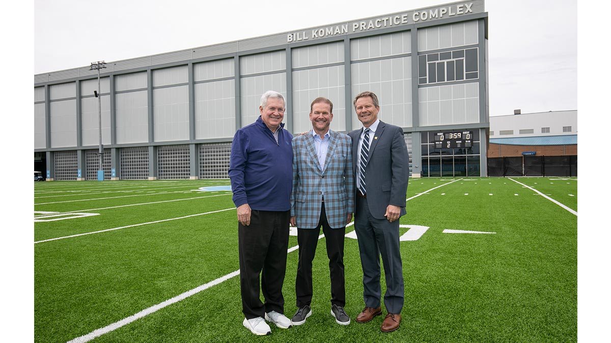 Three men stand by the football practice facility.