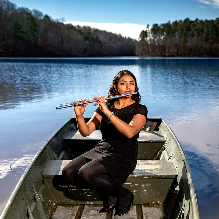 A woman plays the flute on a boat in a lake.