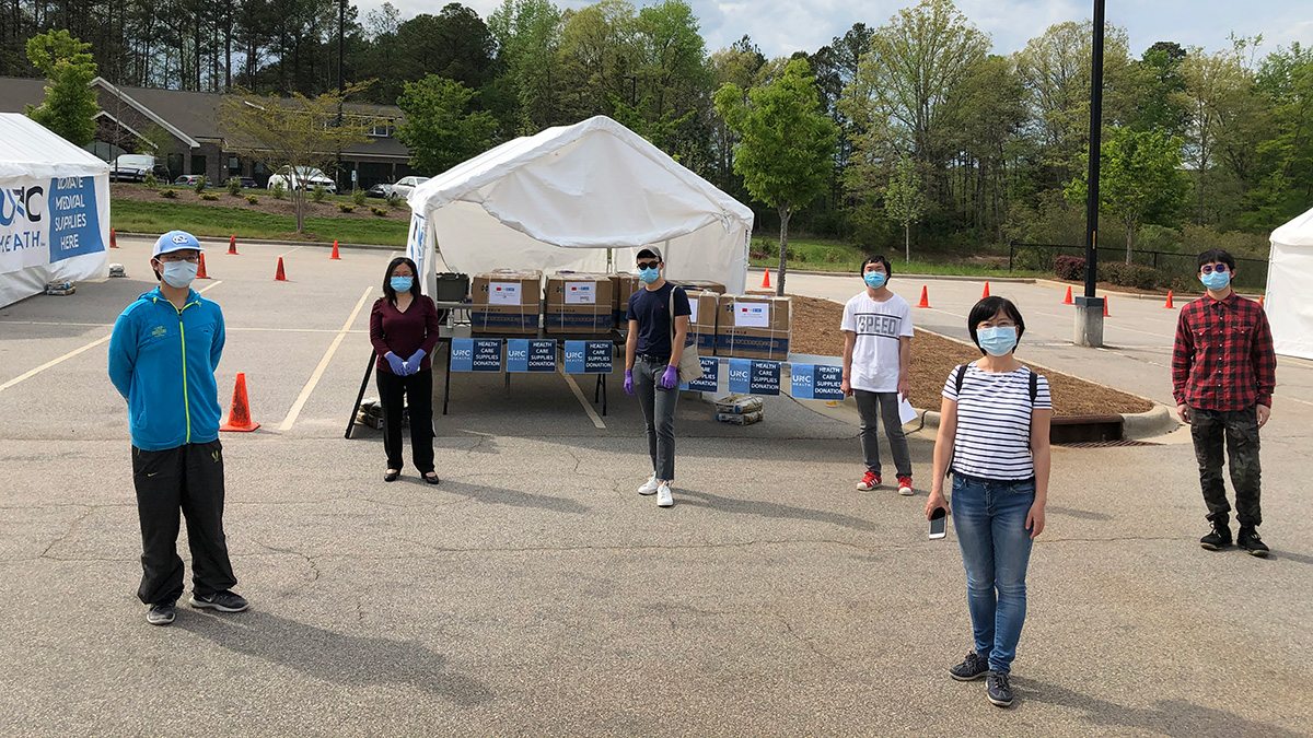 Five students wearing masks stand near boxes of medical masks.