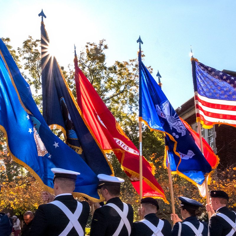 Flags of various military branches being held by ROTC Cadets.