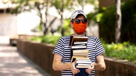 A student wearing a mask carries books.