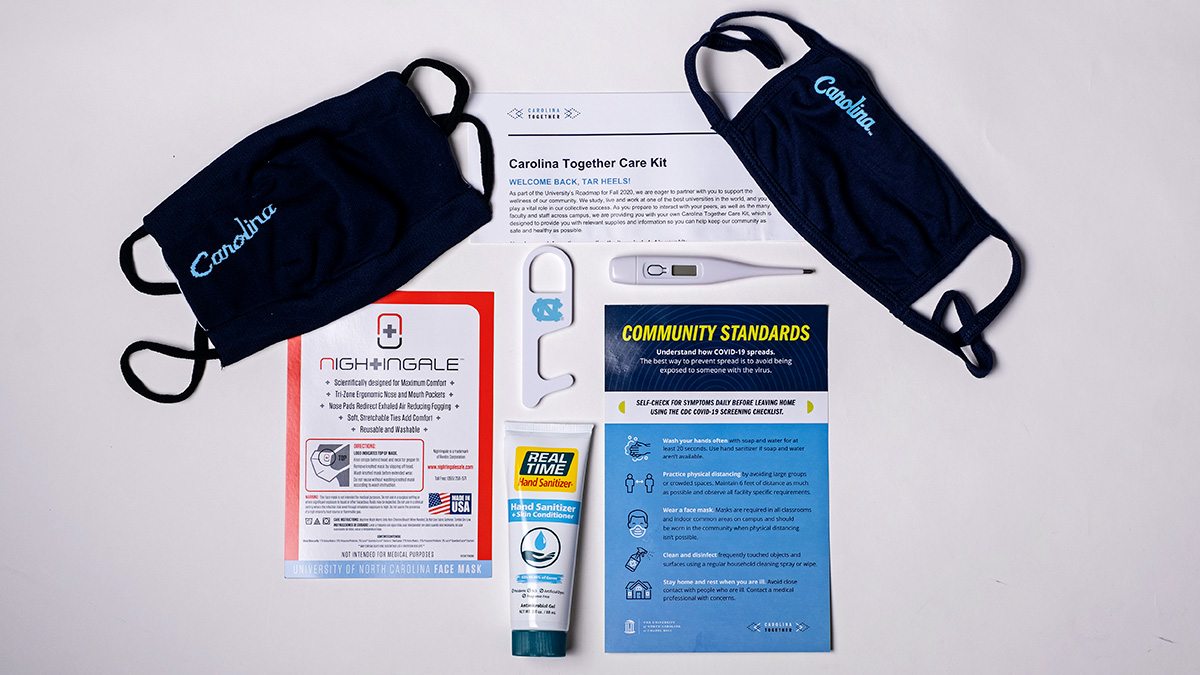 Two masks, a bottle of hand sanitizer, a thermometer and pieces of paper with health instructions on a table.