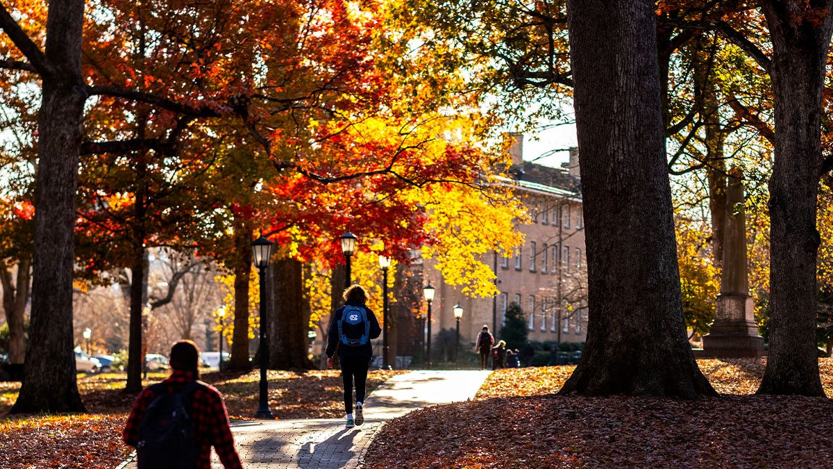 Students walking on a brick pathway on the campus of UNC-Chapel Hill surrounded by trees with yellow-, red- and orange-colored