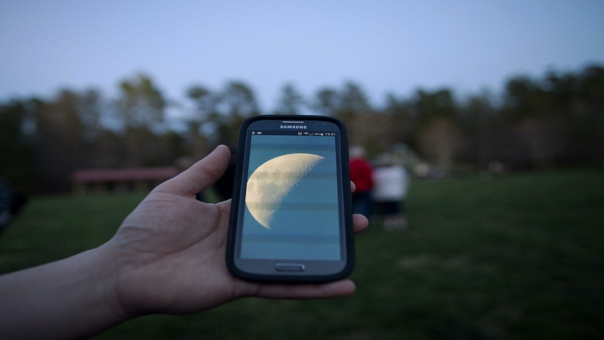 A hand holds a cell phone with the picture of a moon on it.