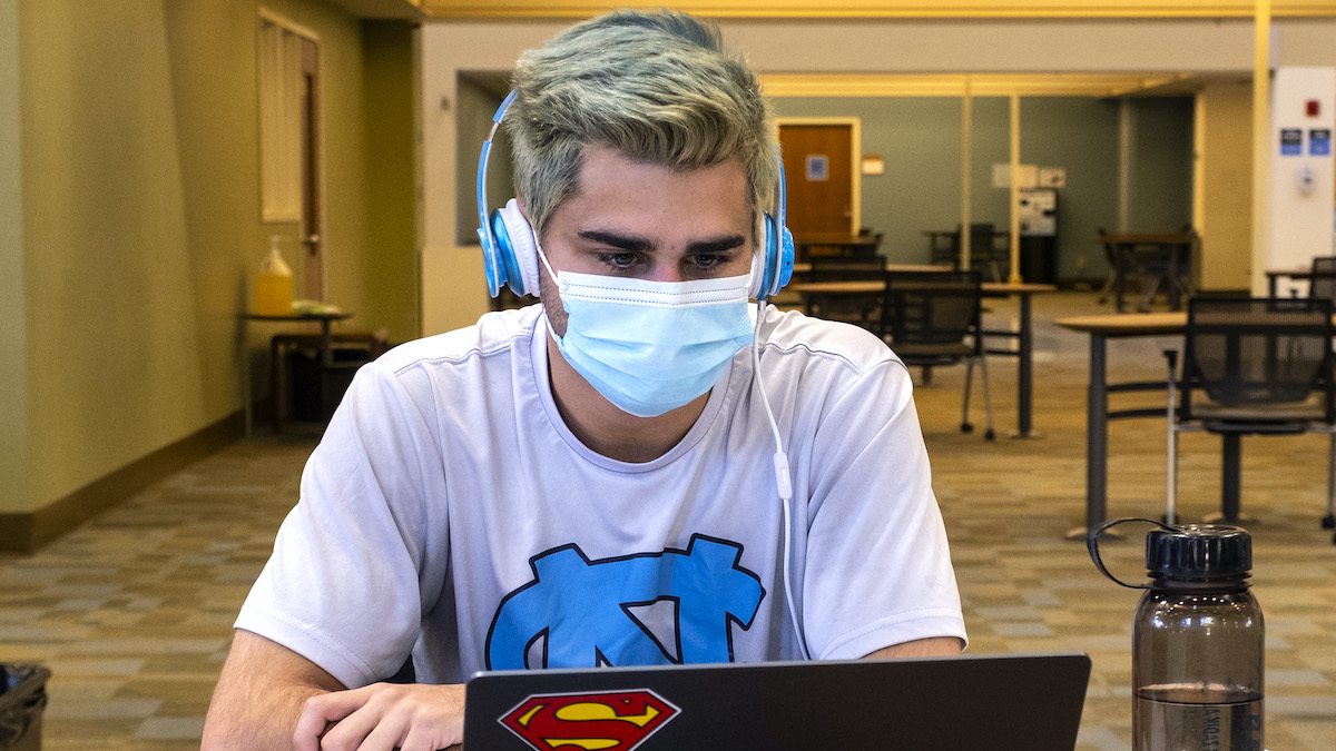 A masked student listens to headphones in Davis library.