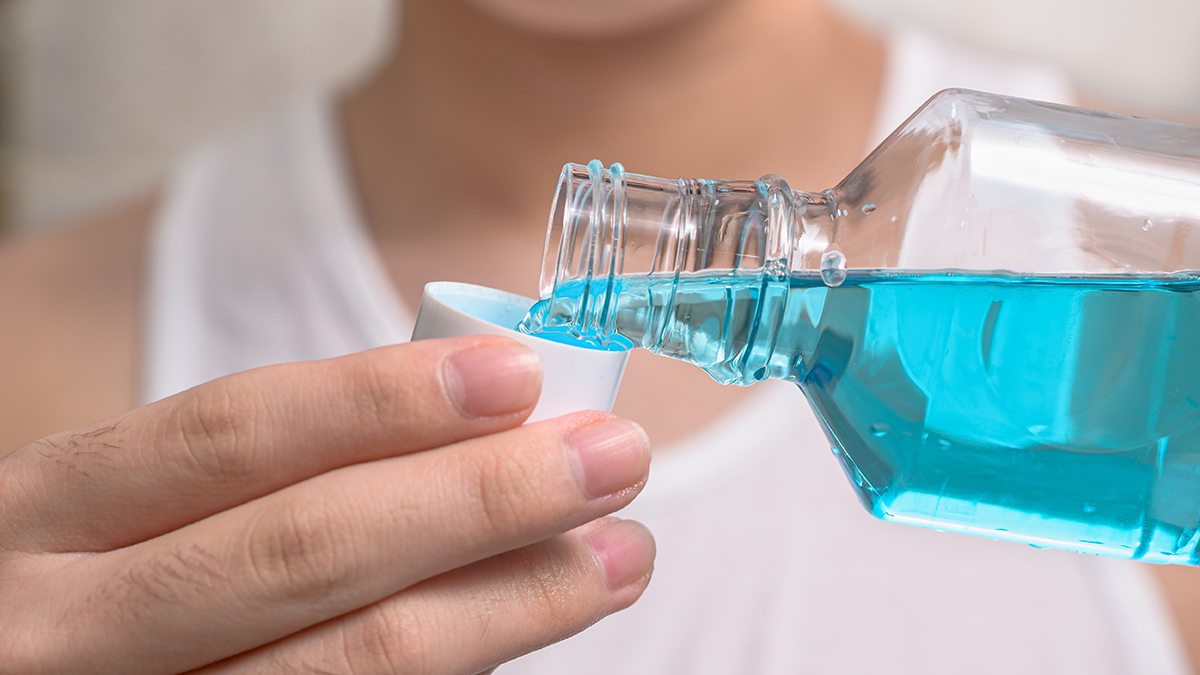 A person pours blue mouthwash into a lid.