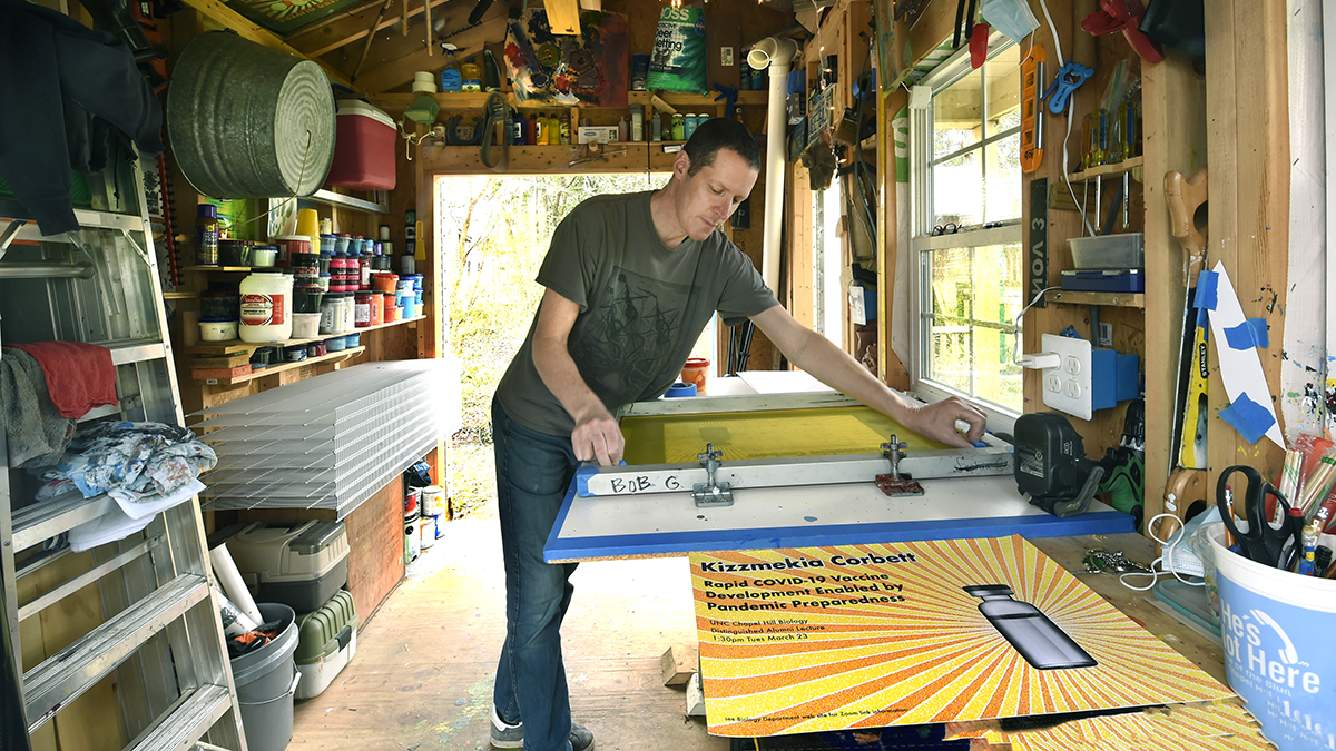 Bob Goldstein working on a screenprinting press in a shed.
