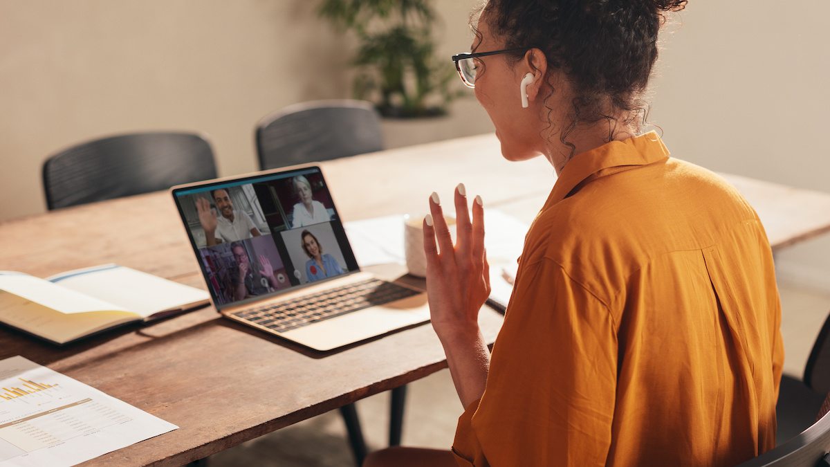 A young woman waves at people joining a video conference call.