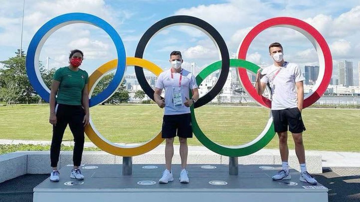 Three men standing near the Olympic rings.
