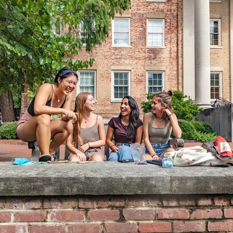 Four students sitting on a bench together in front of South Building.