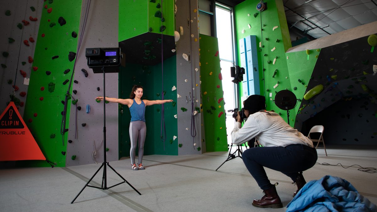 A Carolina student takes a photo of a climber in front of a rock wall.