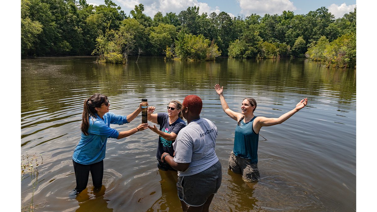 Four women standing in a lake collecting water samples.