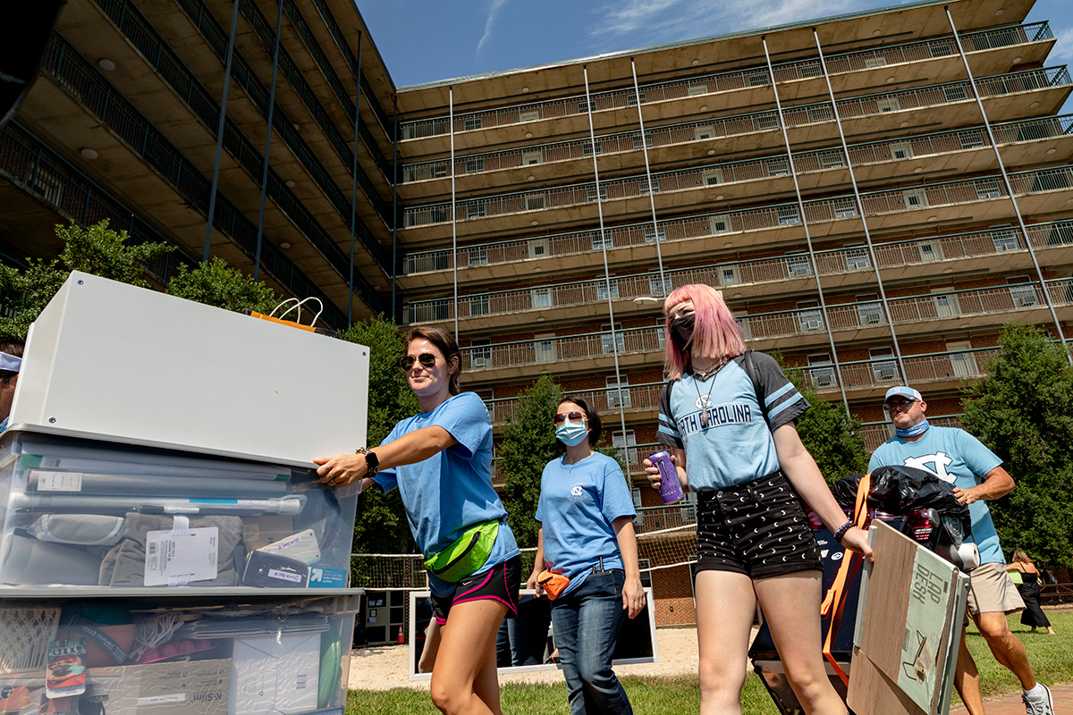 A group of students roll boxes in front of Hinton James residence hall.