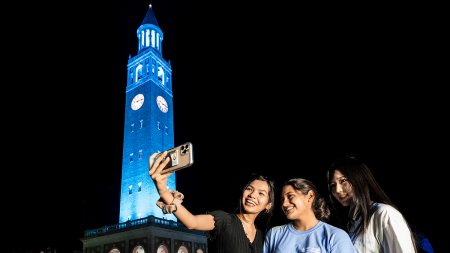 Students pose for a selfie in front of a blue-lit Bell Tower.