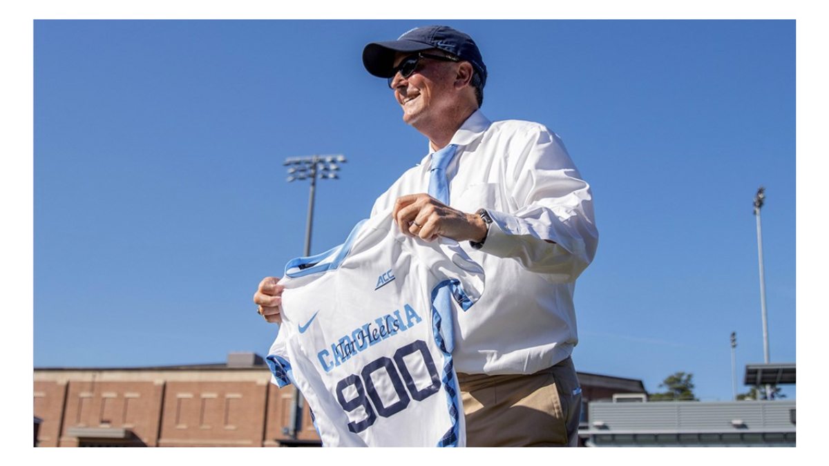 Anson Dorrance holds a Carolina women's soccer jersey with the number 900.