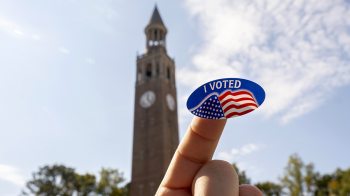 A "I voted sticker" being held up by the Bell Tower.