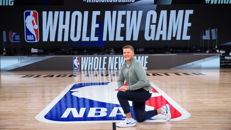 Jake Mendys on the basketball court with the NBA logo behind him.