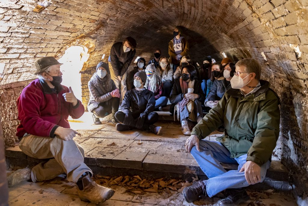Steponaitis, Hewitt and the students gather inside the firing kiln to discuss the different temperature levels pottery can be baked at.