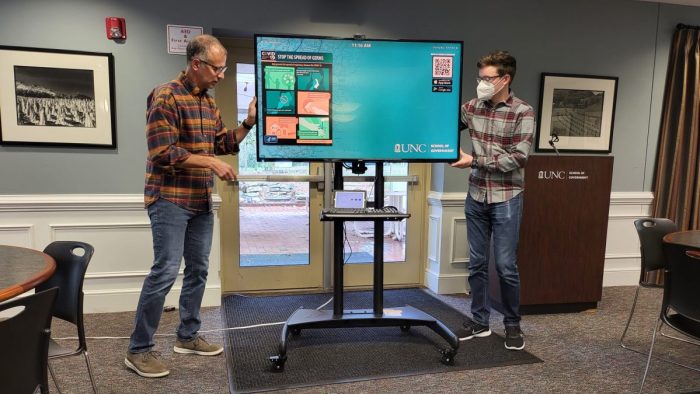 Two people move a screen on a stand.