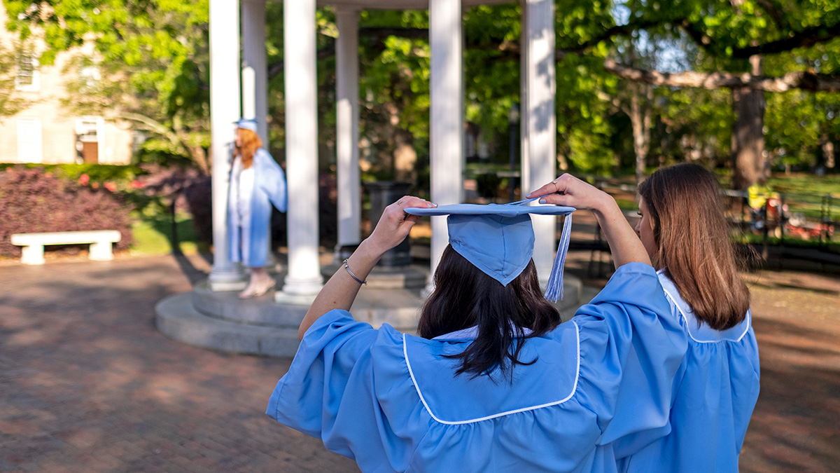 A student adjusts their cap by the old well