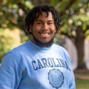 Daniel Garcia in blue Carolina pullover with trees in background