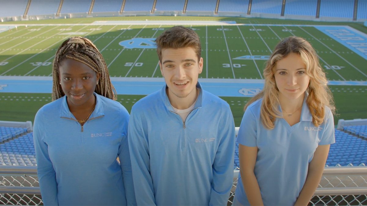 Three students in Visitors Center shirts stand in Kenan Stadium.