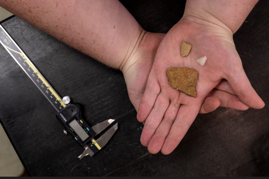 Mauney holds a pottery sherd , stone projectile point and part of a pipe bowl 