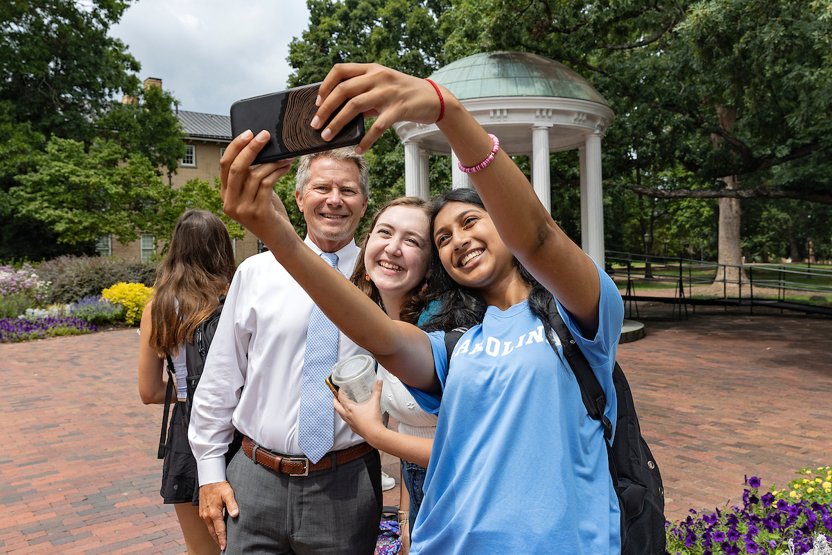 Chancellor Guskiewicz takes a selfie with two students in front of the Old Well