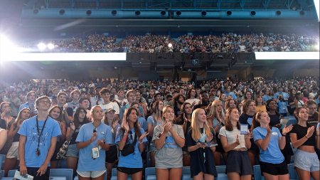 Students standing in the Dean Smith Center at the end of convocation