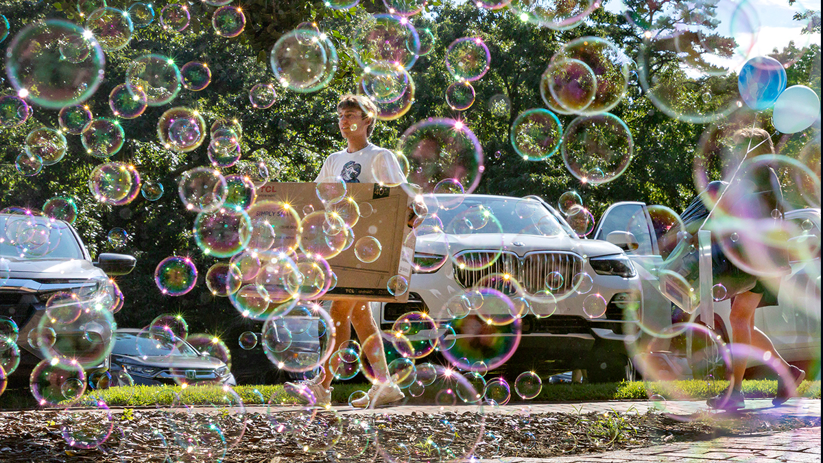 A student carries a television while a bubble blower runs