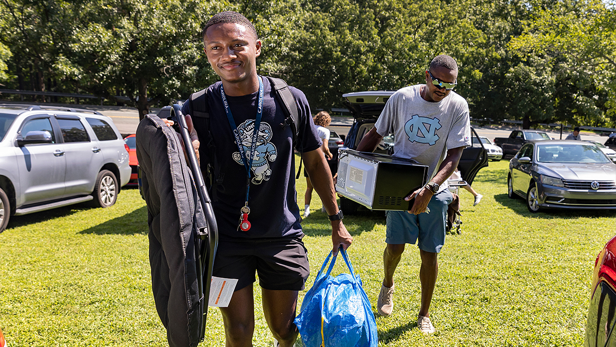 A student and his father carry bags and boxes into Hinton James dorm