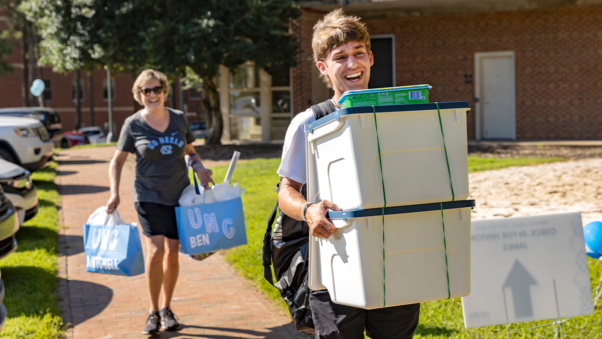 A student and his mother carry boxes and gift bags into Hinton James