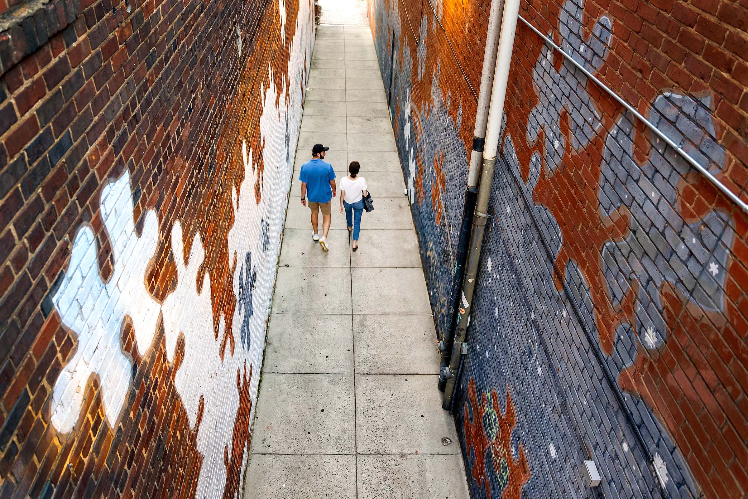 Two people walk in an alley with a mural of puzzle pieces on the side.